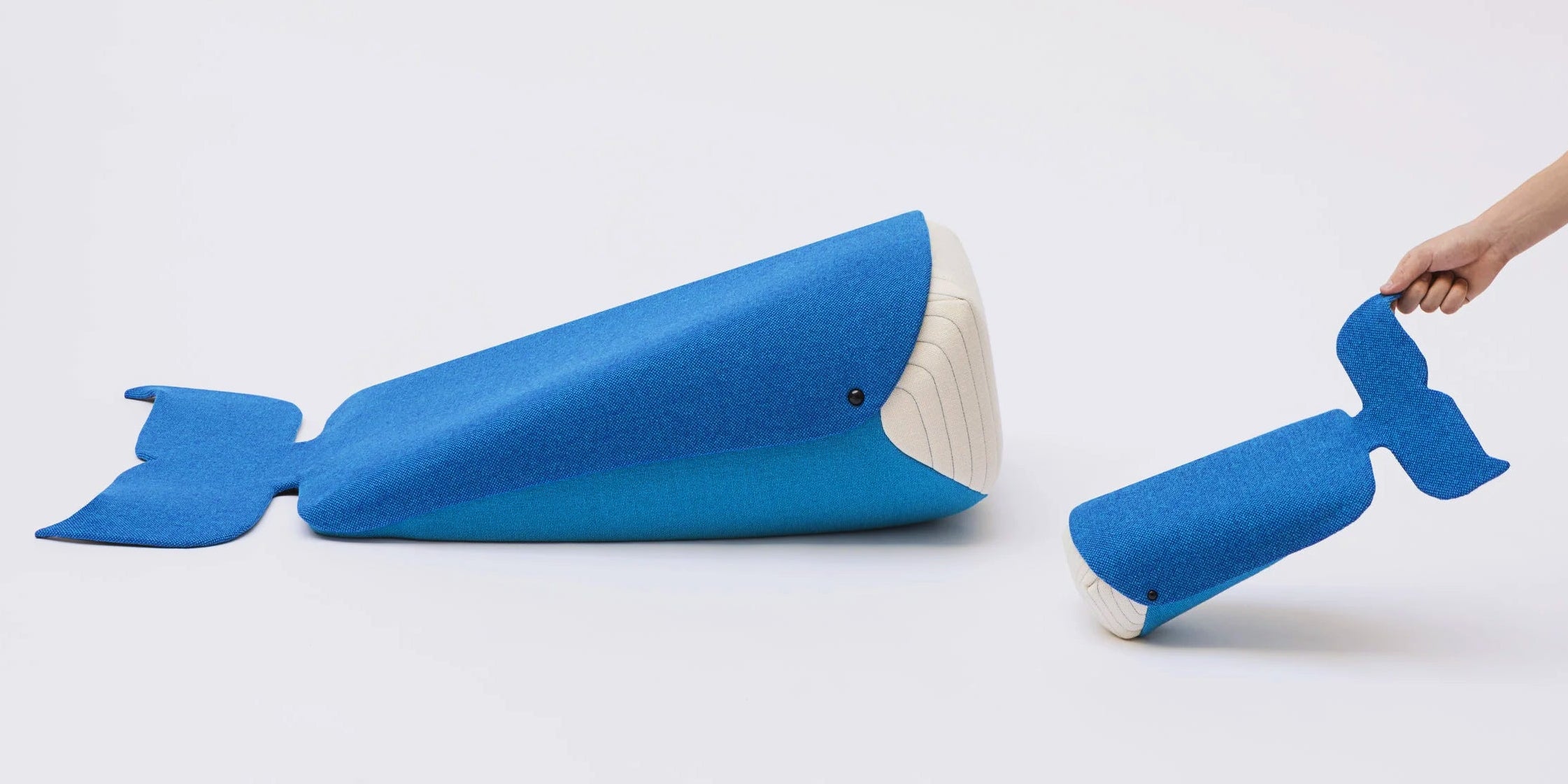 Blue whale-shaped pillow with a smaller version held by a hand on a white background